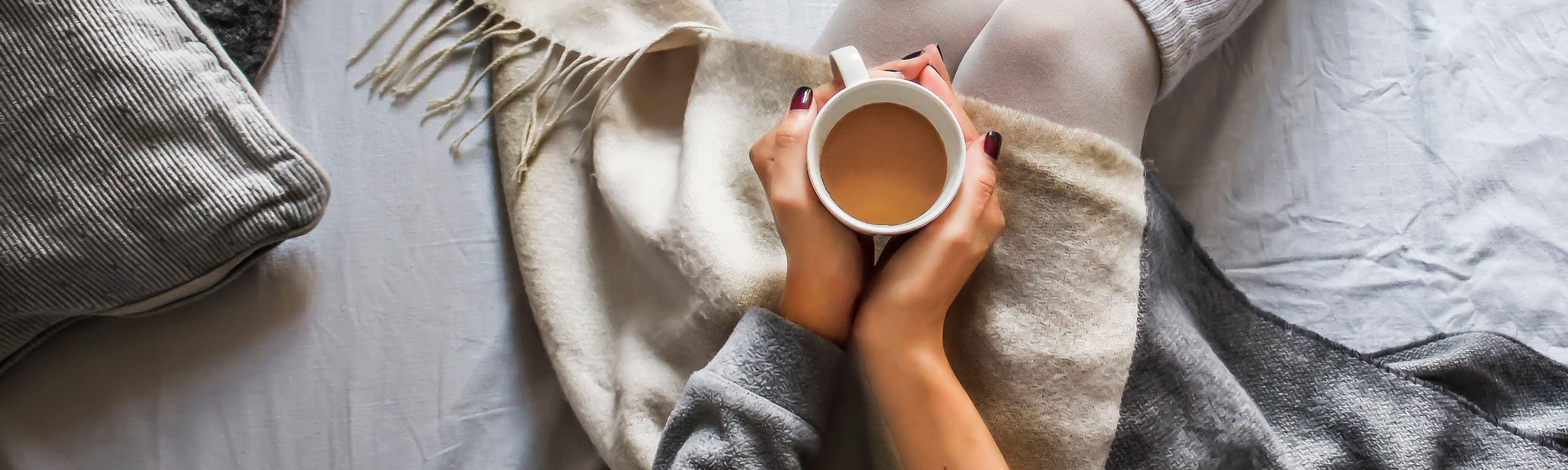 A woman's hands wrapped around a cup of coffee sitting in her lap.